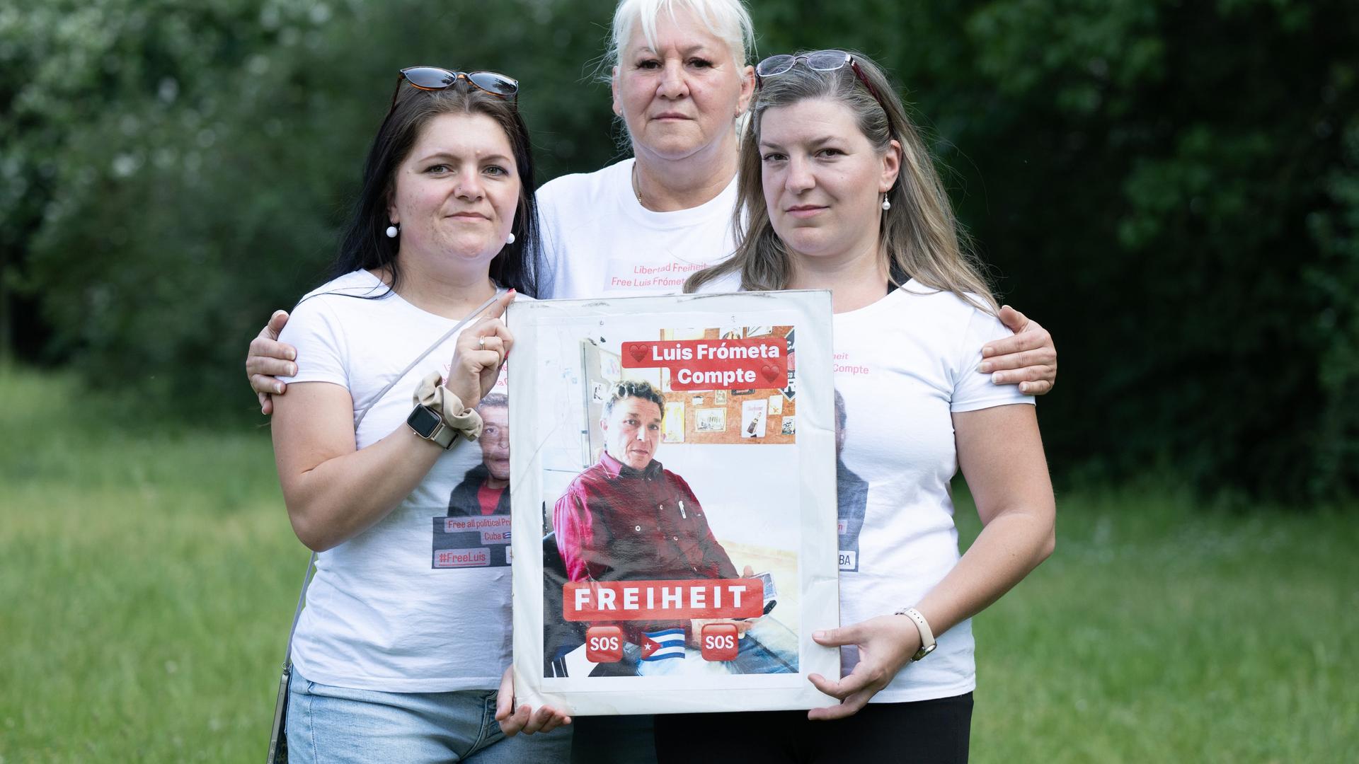 Maria (l) und Janie (r) Frometa Compte, Töchter des inhaftierten Deutsch-Kubaners Luis Frómeta Compte, und Silke Frometa Compte (M), Ehefrau, halten ein Foto von Luis Frometa Compte.