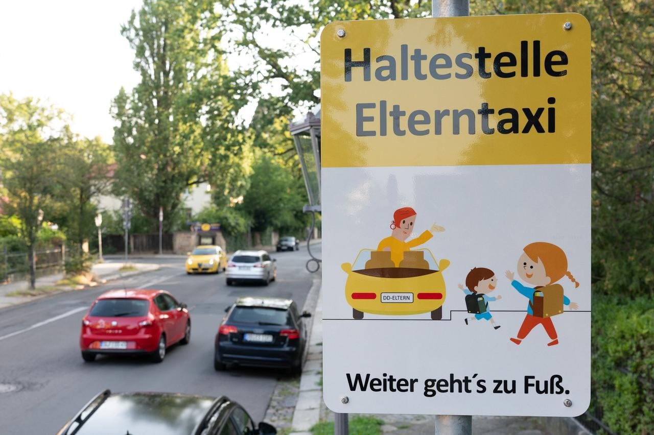 Ein Schild mit der Aufschrift "Haltestelle Elterntaxi" steht vor einer Grundschule. 