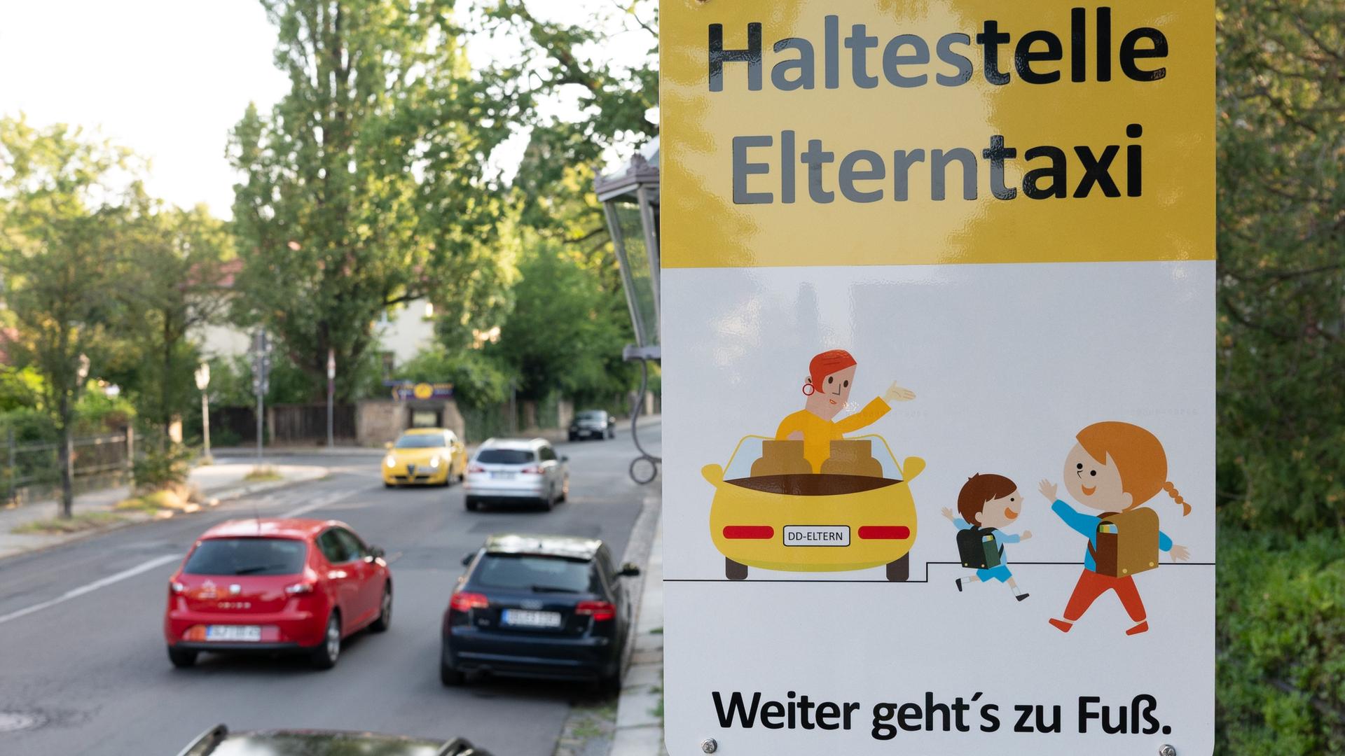 Ein Schild mit der Aufschrift "Haltestelle Elterntaxi" steht vor einer Grundschule. Ein Schild mit der Aufschrift "Haltestelle Elterntaxi" steht vor einer Grundschule.
