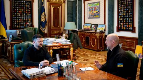 Selenskyj und Shmyal sitzen in einem Büro gemeinsam zu einer Besprechung am Schreibtisch.