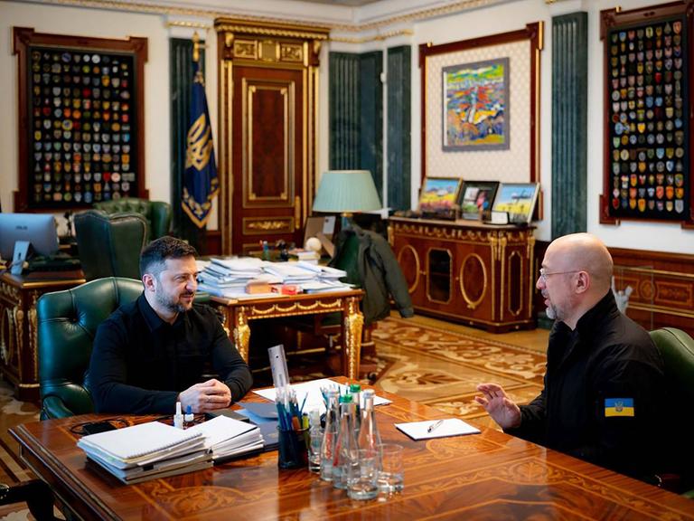 Selenskyj und Shmyal sitzen in einem Büro gemeinsam zu einer Besprechung am Schreibtisch.