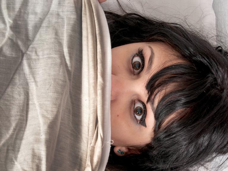 Eine Frau liegt mit offenen Augen im Bett.