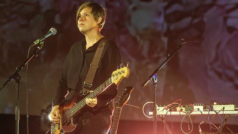 Wir sehen eine Frau, die auf der Bühne steht und E-Gitarre spielt.