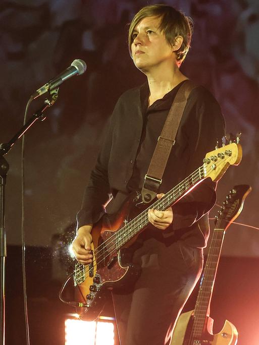 Wir sehen eine Frau, die auf der Bühne steht und E-Gitarre spielt.