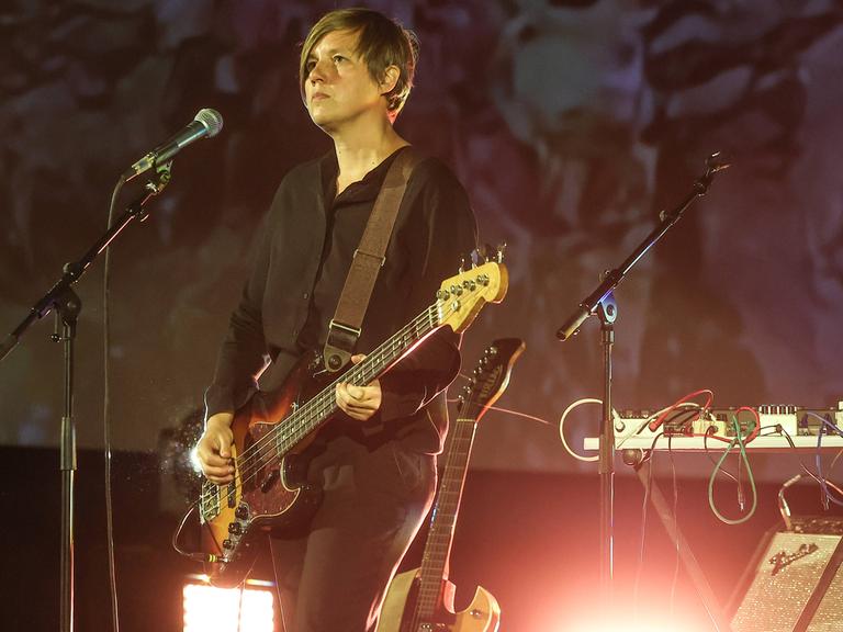 Wir sehen eine Frau, die auf der Bühne steht und E-Gitarre spielt.