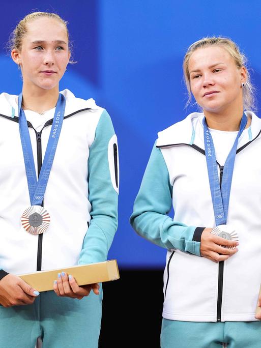 Die russischen Tennisspielerinnen Mirra Andreeva und Diana Shnaider tragen bei der Medaillenzeremonie die Kleidung der neutralen individuellen Athlet:innen.