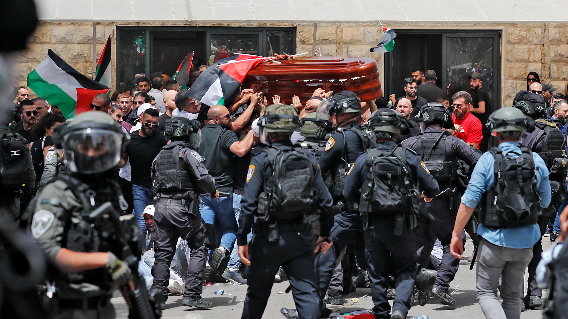 Männer, die Palästinenser-Flaggen in der Hand haben, tragen einen Sarg. Im Vordergrund sieht man Sicherheitskräfte.