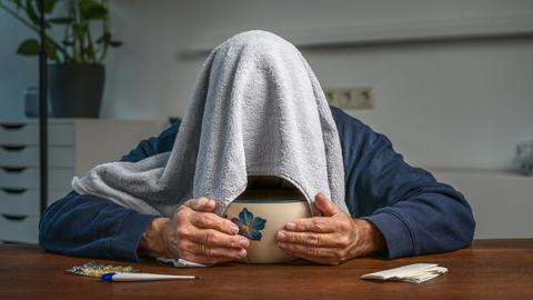 Mann mit einem Handtuch über dem Kopf bei der Dampfinhalation über einer Schüssel