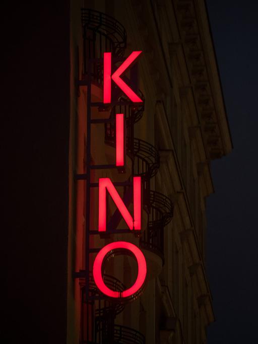 Der Schriftzug KINO steht als Leuchtreklame an einer Hausfassade in der Abenddämmerung.