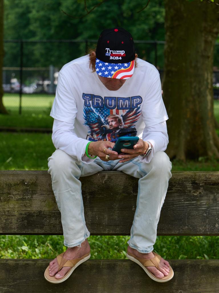 Mann mit Trump-Shirt und Basecap sitzt auf Rückenlehne einer Bank und blickt aufs Smartphone (25.5.2024). Mann mit Trump-Shirt und Basecap sitzt auf Rückenlehne einer Bank und blickt aufs Smartphone (25.5.2024).