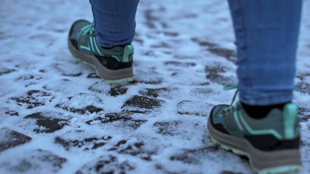 Das Bild zeigt einen frostigen, gepflasterten Boden. 2 Füße in Turn-Schuhen bewegen sich vorsichtig auf dem Boden. 