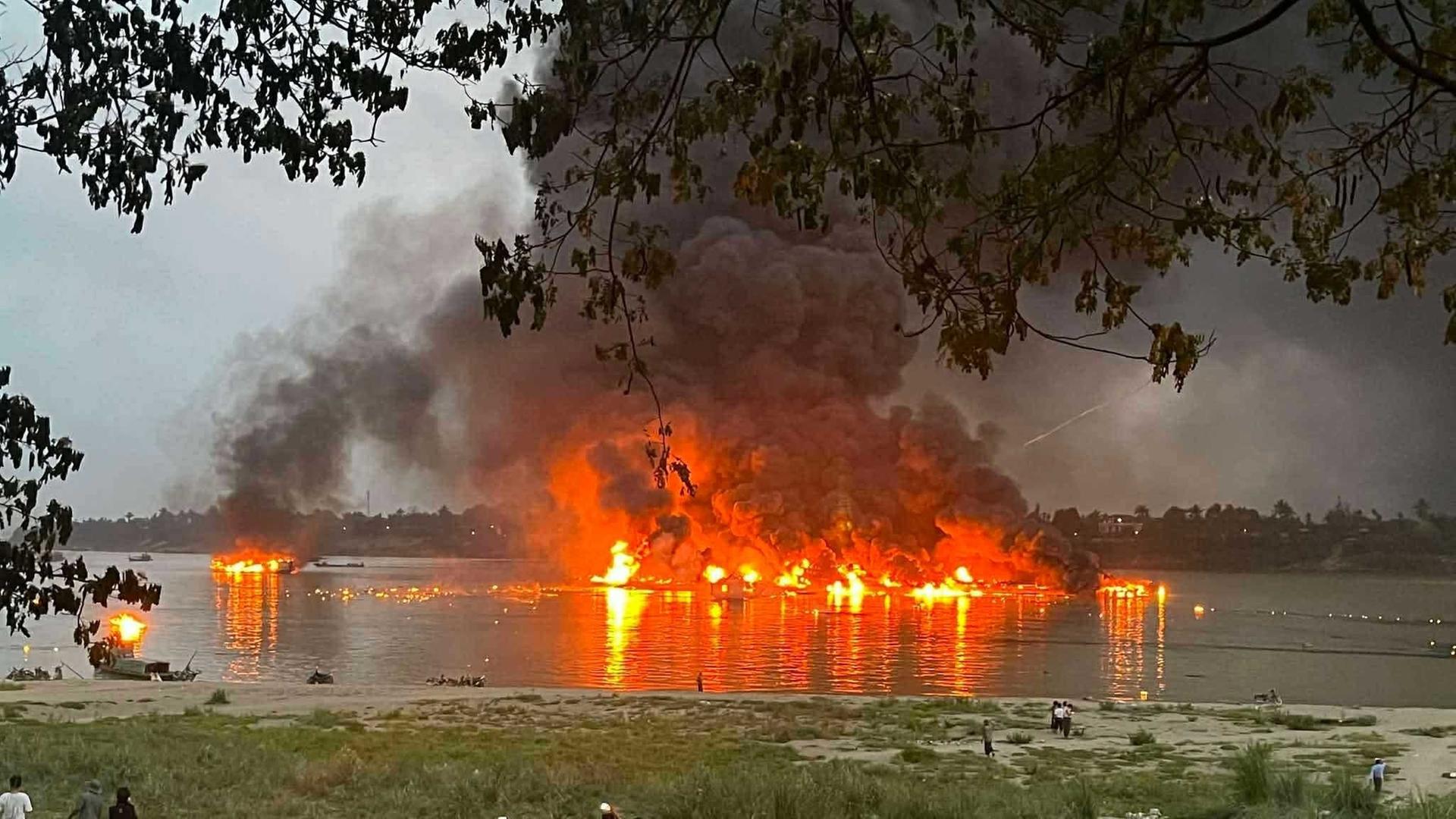 Mehrere Schiffe stehen im Hafen von Homalin in Myanmar in Flammen. Es steigen schwarze Rauchwolken auf.