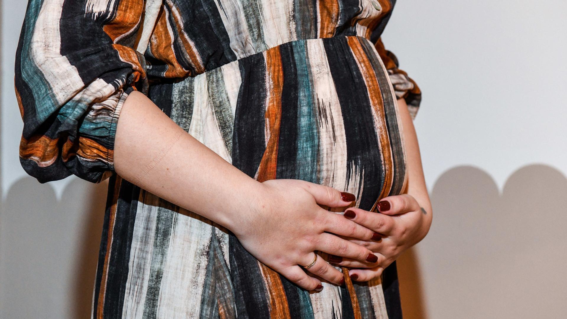 Eine schwangere Frau hat die Hände vor ihrem Bauch verschränkt.