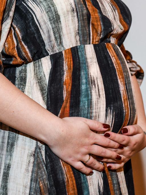 Eine schwangere Frau hat die Hände vor ihrem Bauch verschränkt.