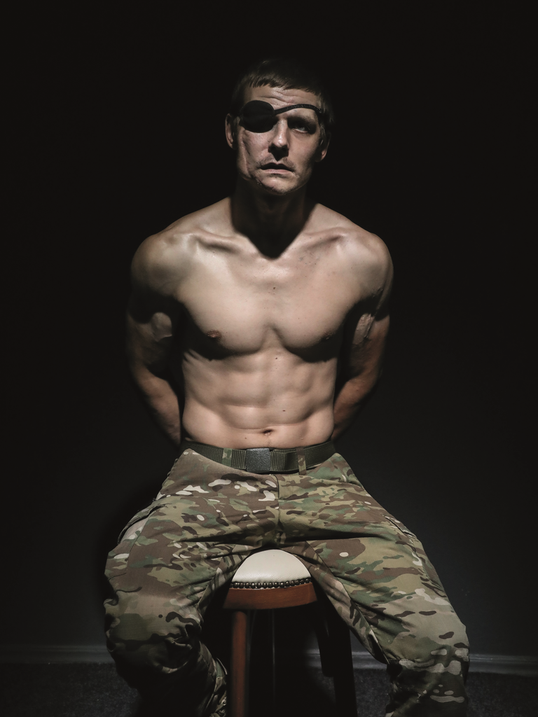 Der verwundete ukrainische Soldat Wolodymyr Melnik sitzt mit nacktem Oberkörper in einem dunklen Fotostudio. Er trägt eine Augenklappe.