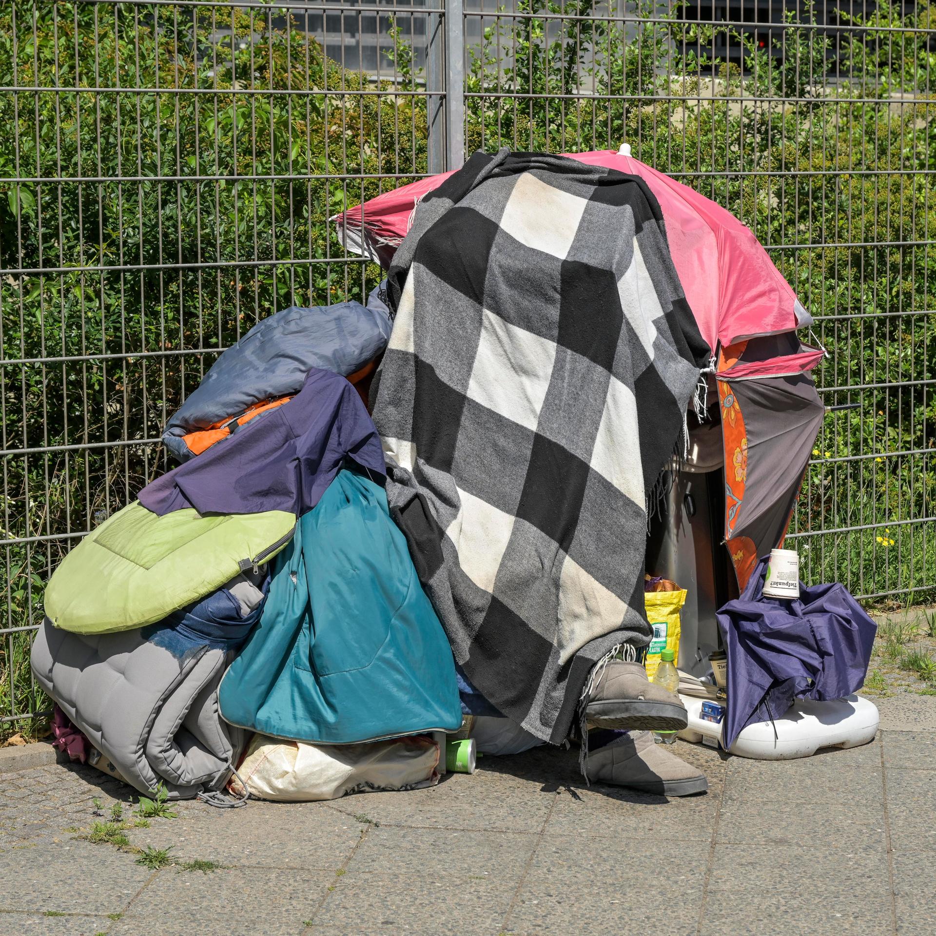 Eine wohnungslose Person in Berlin schützt sich gegen die Sonne mit Decken über dem Kopf.