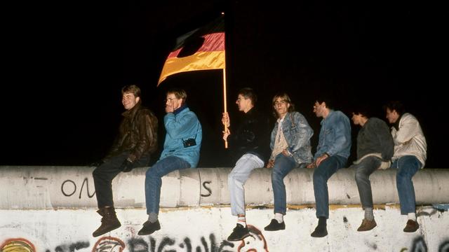 In der Nacht des 9. November 1989 sind Menschen mit einer zerschnittenen DDR-Fahne auf die Berliner Mauer am Brandenburger Tor geklettert.