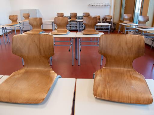 Ein leeres Klassenzimmer. Die Holzstühle wurden auf die weißen Tische gestellt. 