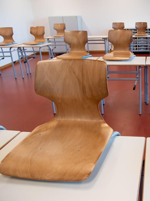 Ein leeres Klassenzimmer. Die Holzstühle wurden auf die weißen Tische gestellt. 