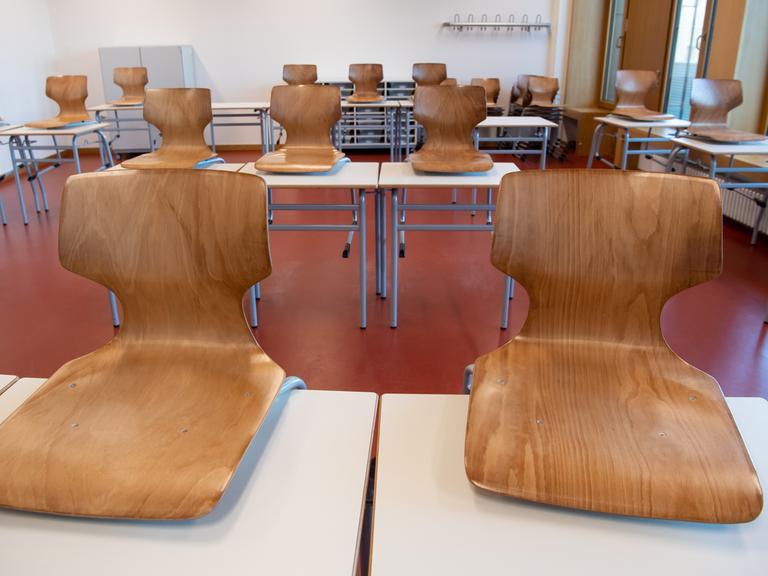 Ein leeres Klassenzimmer. Die Holzstühle wurden auf die weißen Tische gestellt. 