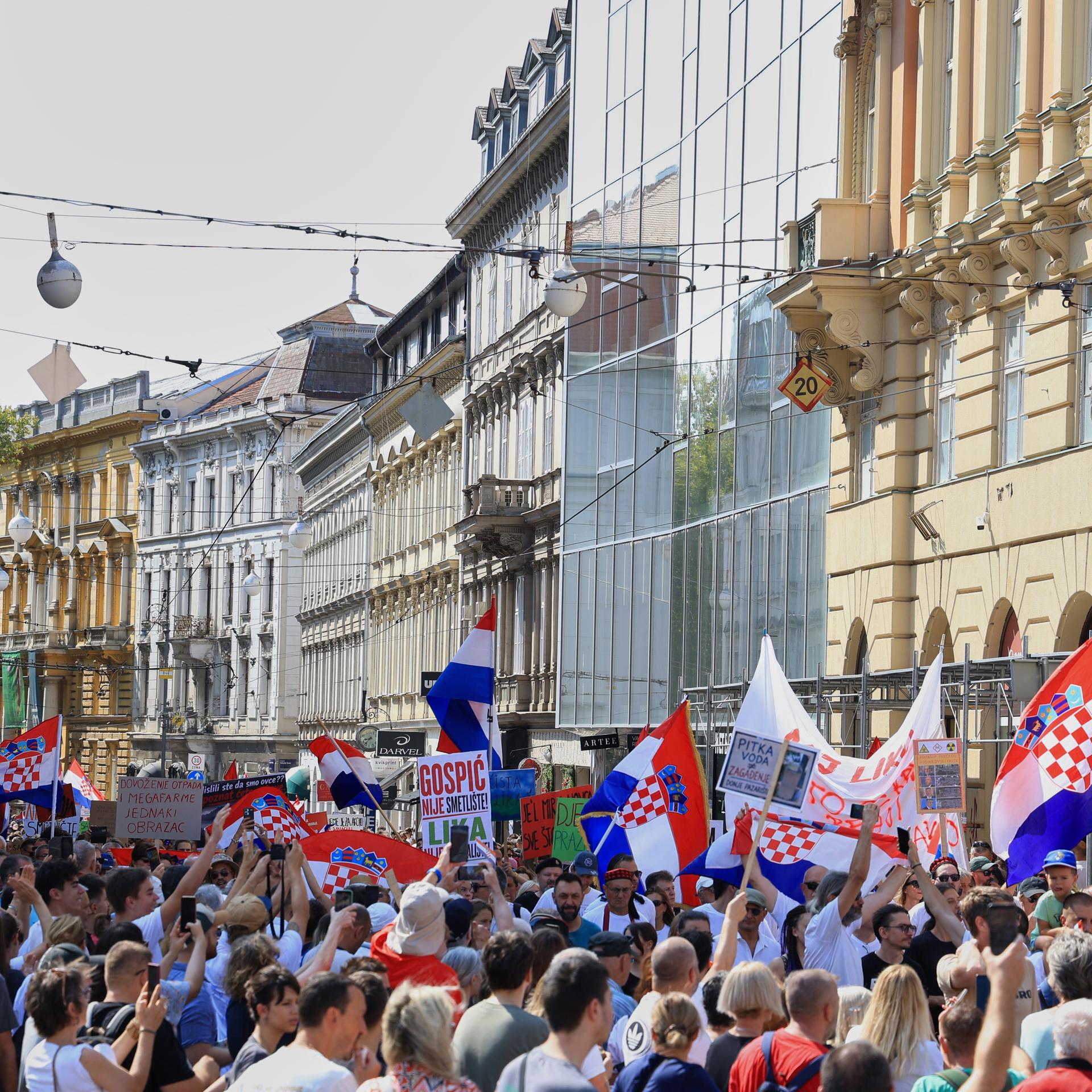 Ein große Menschengruppe steht in einer Straße mit alten Häusern und schwenkt kroatische Flaggen. 