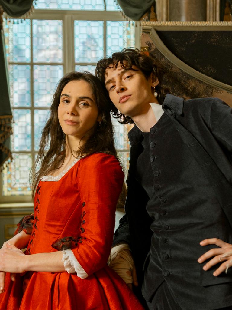 Die Schauspieler Havana Joy und Eren M. Güvercin stehen in barocken Kostümen als Geschwister Mozart vor einem aufgeklappten Cembalo.