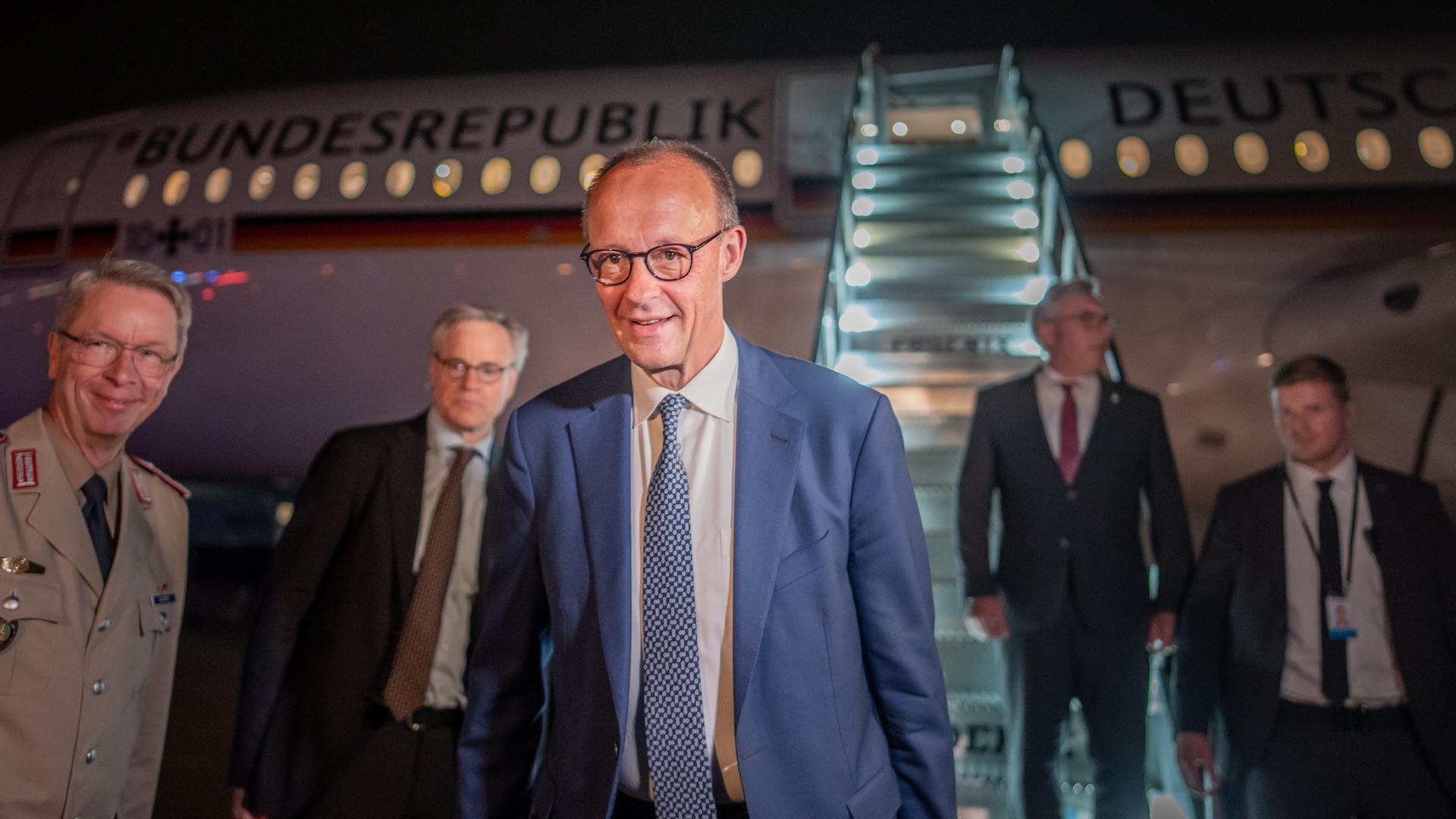 Das Bild zeigt Bundeskanzler Merz und vier Begleitpersonen vor einem Flugzeug der Flugbereitschaft.