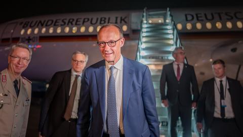 Das Bild zeigt Bundeskanzler Merz und vier Begleitpersonen vor einem Flugzeug der Flugbereitschaft.