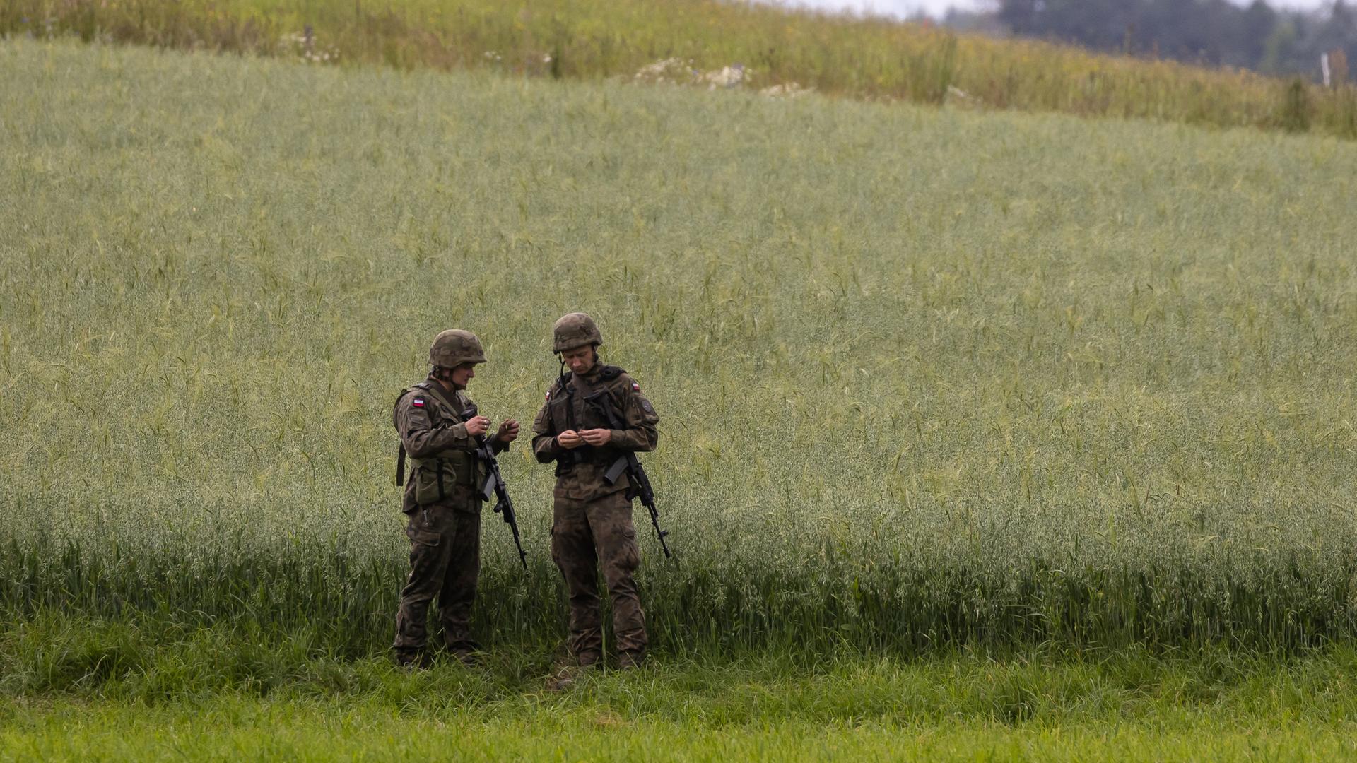 Zwei polnische Soldaten stehen am Rande eines Getreidefeldes.