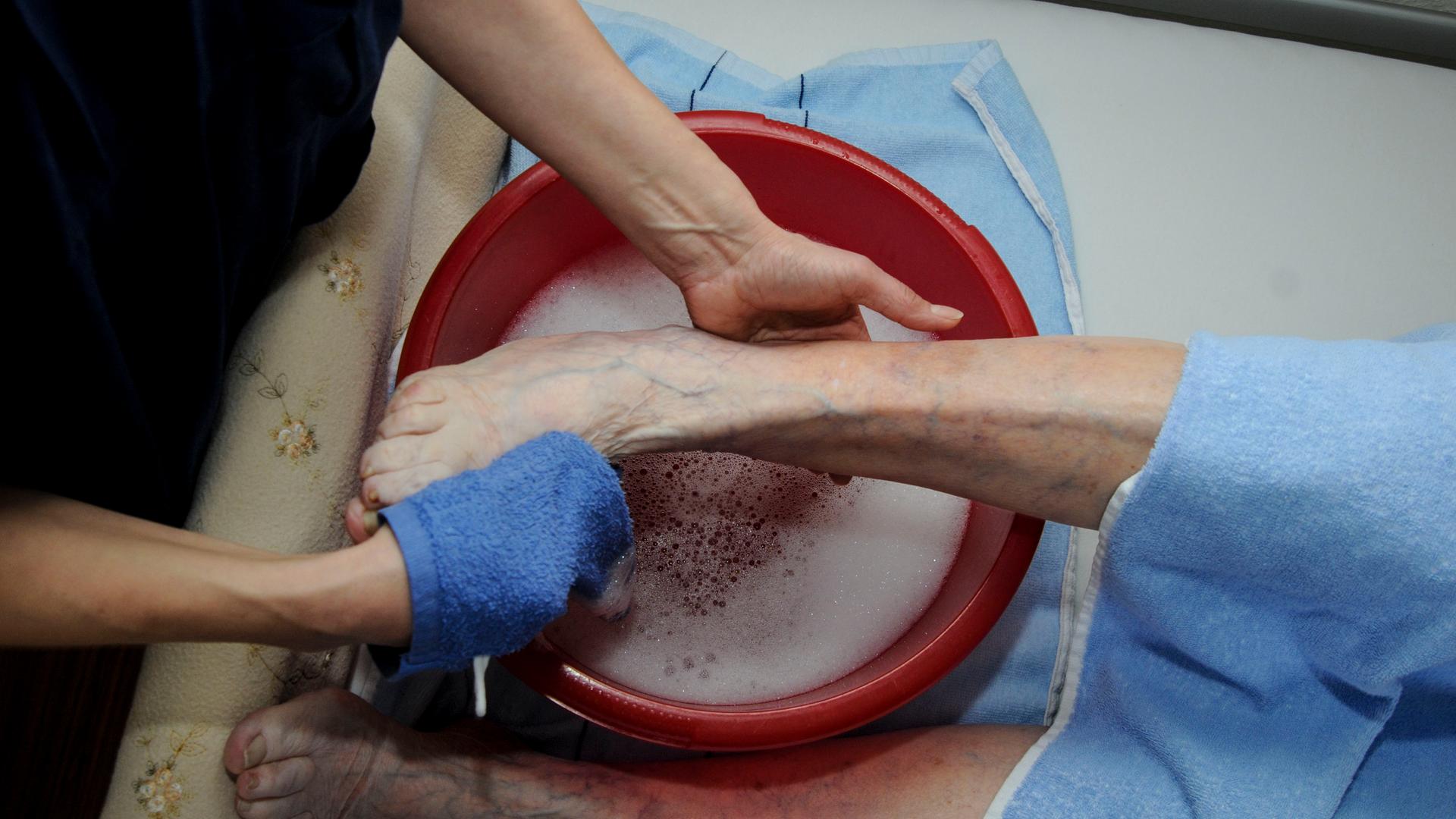 Altenpflege: Einem Patienten werden über einer Schüssel im Bett die Füsse gewaschen.