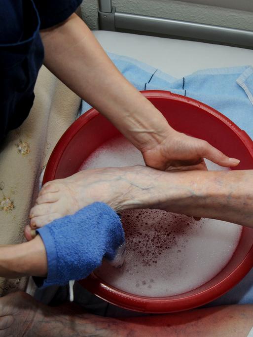 Altenpflege: Einem Patienten werden über einer Schüssel im Bett die Füsse gewaschen.