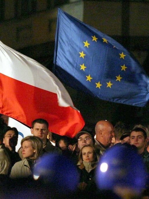 Menschen schwenken eine polnische und eine EU-Flagge bei einem Welcome-To-Europe-Konzert auf dem Zamkowy-Platz in Warschau 2004.
