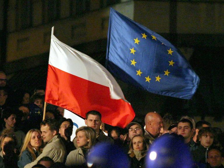 Menschen schwenken eine polnische und eine EU-Flagge bei einem Welcome-To-Europe-Konzert auf dem Zamkowy-Platz in Warschau 2004.