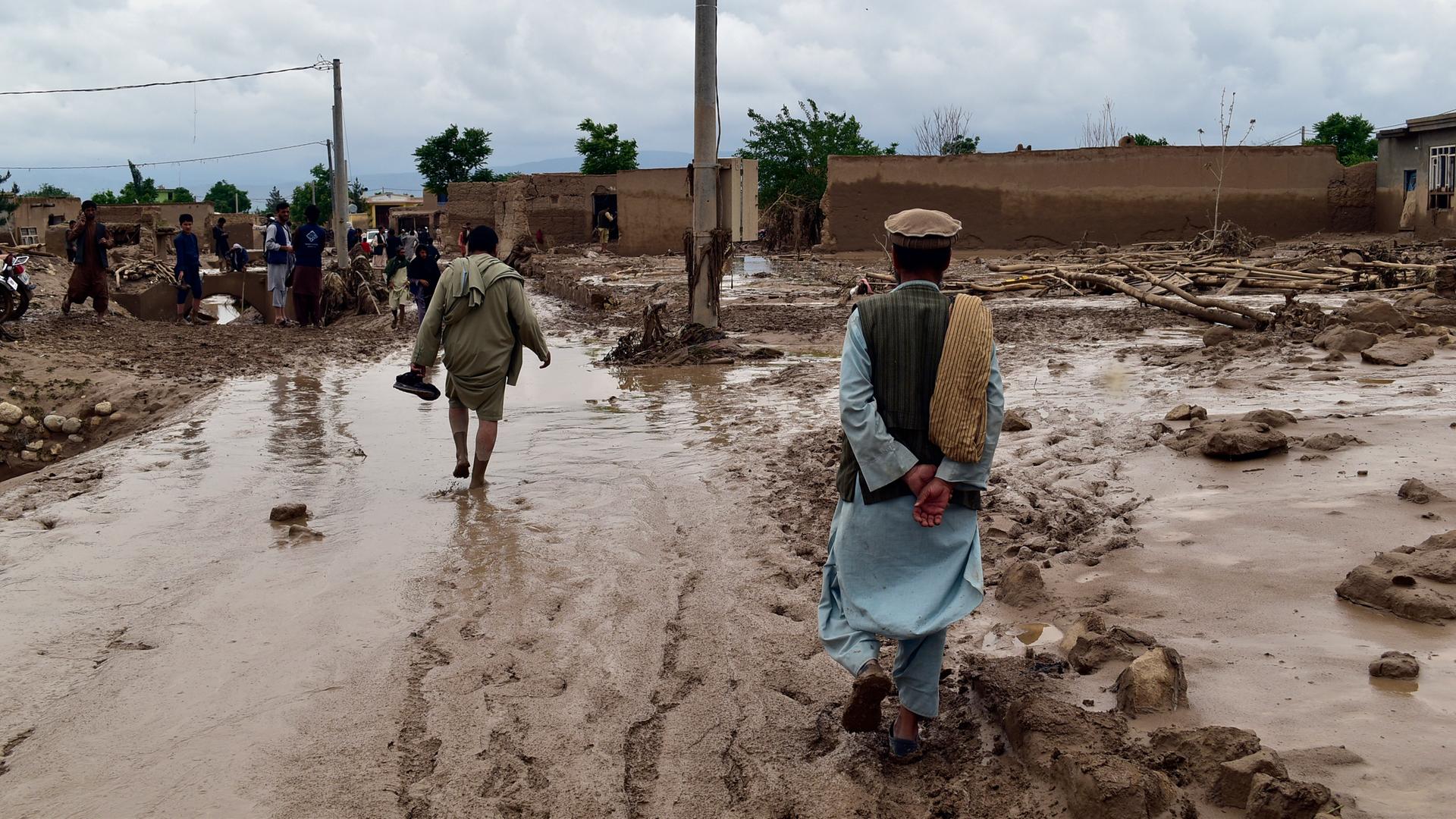 In der nordafghanischen Provinz Baghlan sieht man Menschen in der Nähe ihrer beschädigten Häuser. Sie waten durch den schlammigen Boden. In der nordafghanischen Provinz Baghlan sieht man Menschen in der Nähe ihrer beschädigten Häuser. Sie waten durch den schlammigen Boden.