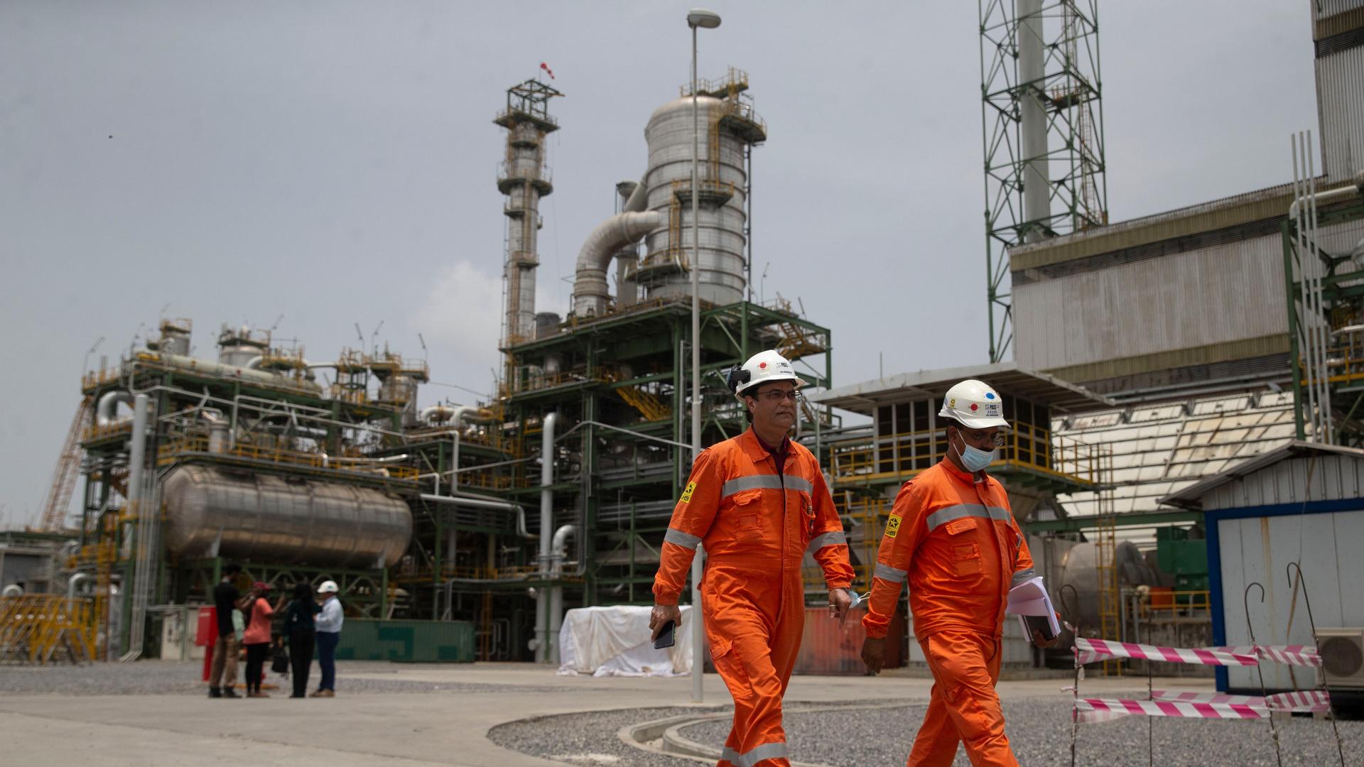 Im Vordergrund gehen zwei Arbeiter entlang, im Hintergrund die Öl-Raffiniere Dangote in der Nähe von Lagos.