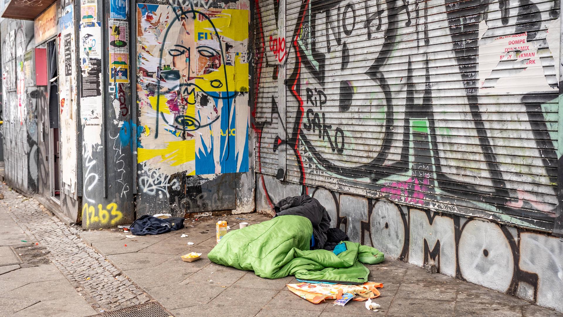 Decken eines Obdachlosen auf der Straße vor einem Supermarkt am Drogen-Hotspot Kottbusser Tor in Berlin Kreuzberg. An den Wänden viele Graffiti