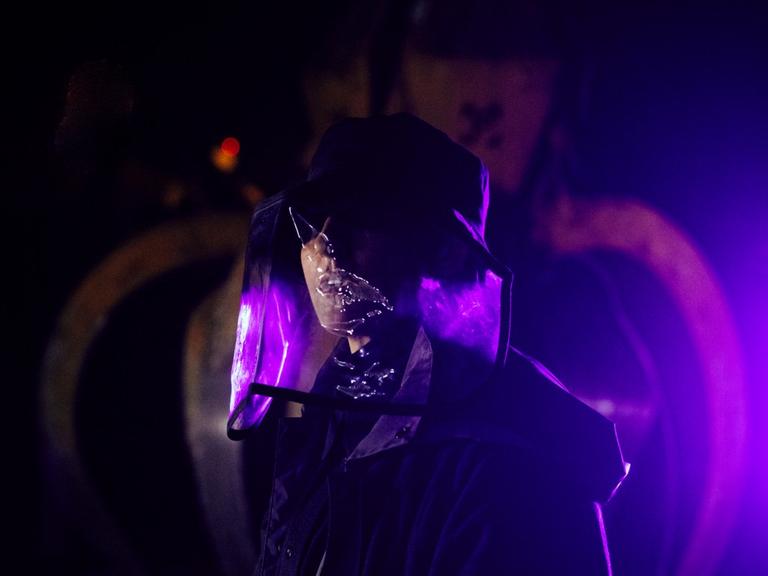Eine Frau mit Hut und Maske in dunkler Szenerie