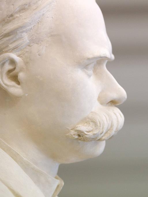 Eine weiße Büste von dem Philosophen Friedrich Nietzsche mit großem Schnurrbart steht im Treppenhaus. Sie ist im Profil zu sehen.