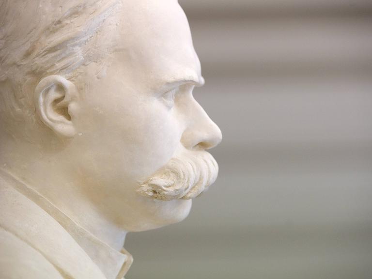 Eine weiße Büste von dem Philosophen Friedrich Nietzsche mit großem Schnurrbart steht im Treppenhaus. Sie ist im Profil zu sehen.
