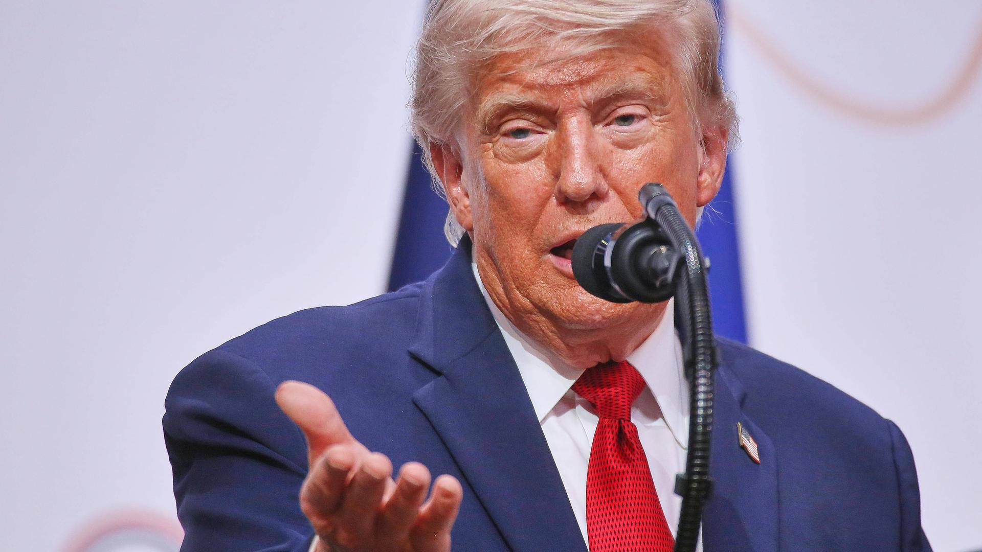 Donald Trump spricht in ein Mikrofon und hebt dabei die rechte Handfläche.