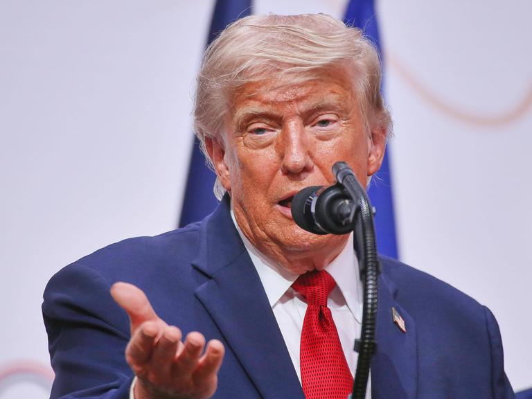 Donald Trump spricht in ein Mikrofon und hebt dabei die rechte Handfläche.