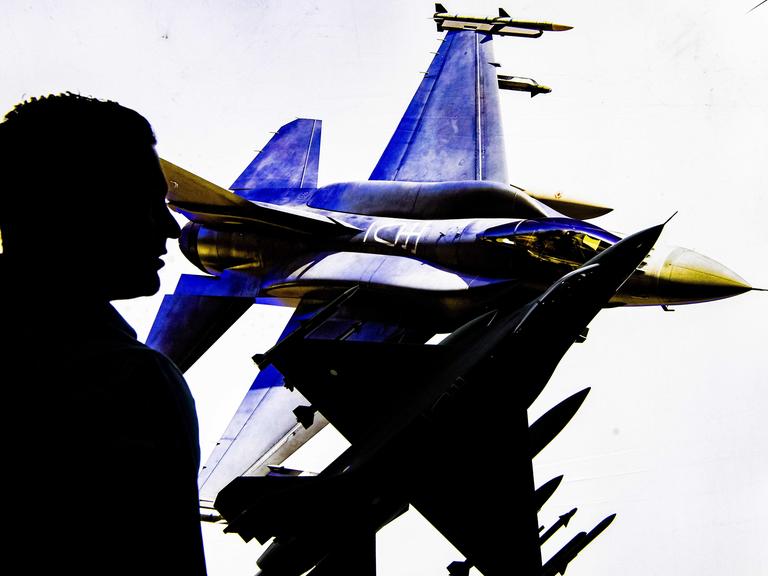 Die Silouette eines Besuchers der Waffenmesse in Ahoi in Rotterdam. Im Hintergrund ist ein Plakat mit Kampfflugzeugen.