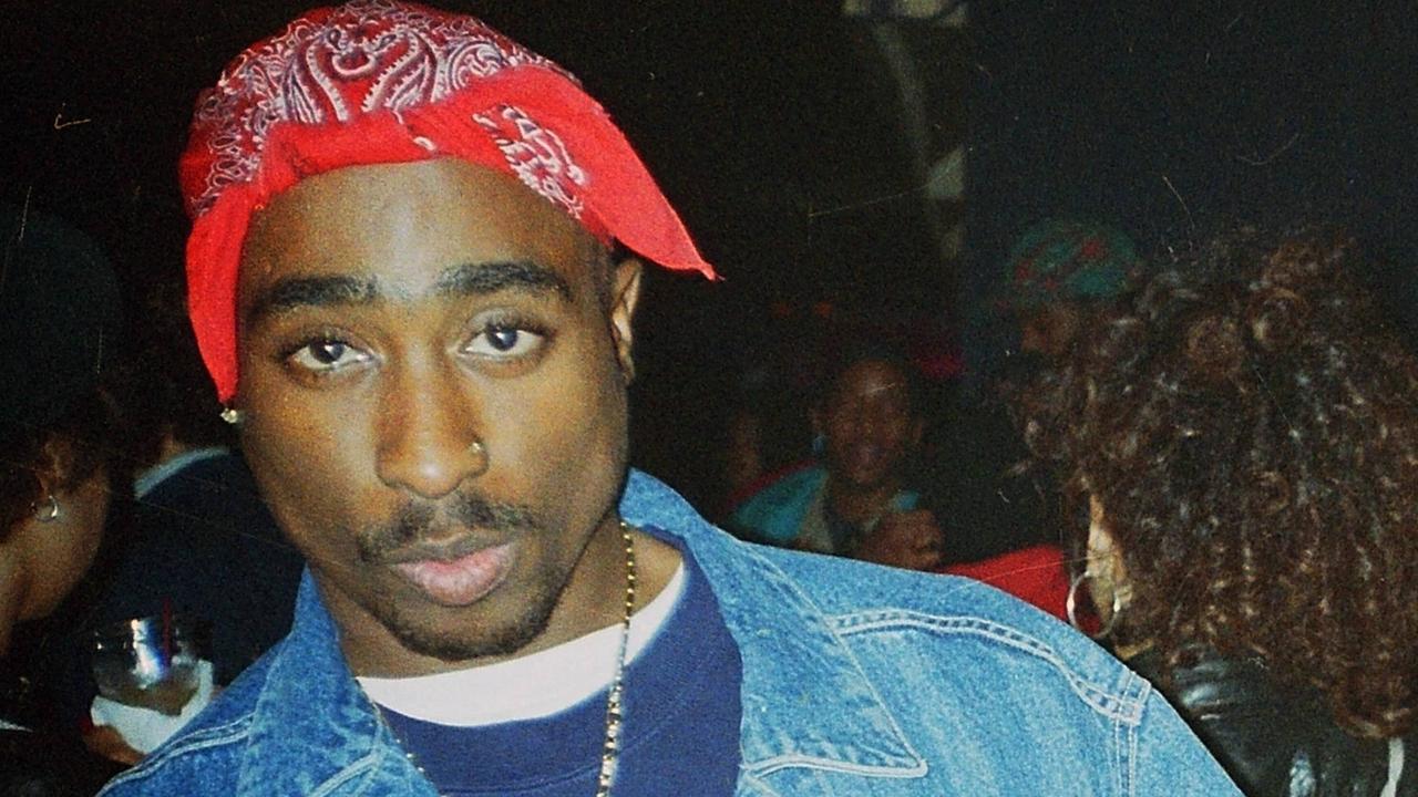 Shakur trägt ein rotes gebundenes Tuch auf dem Kopf. Er schaut in die Kamera.