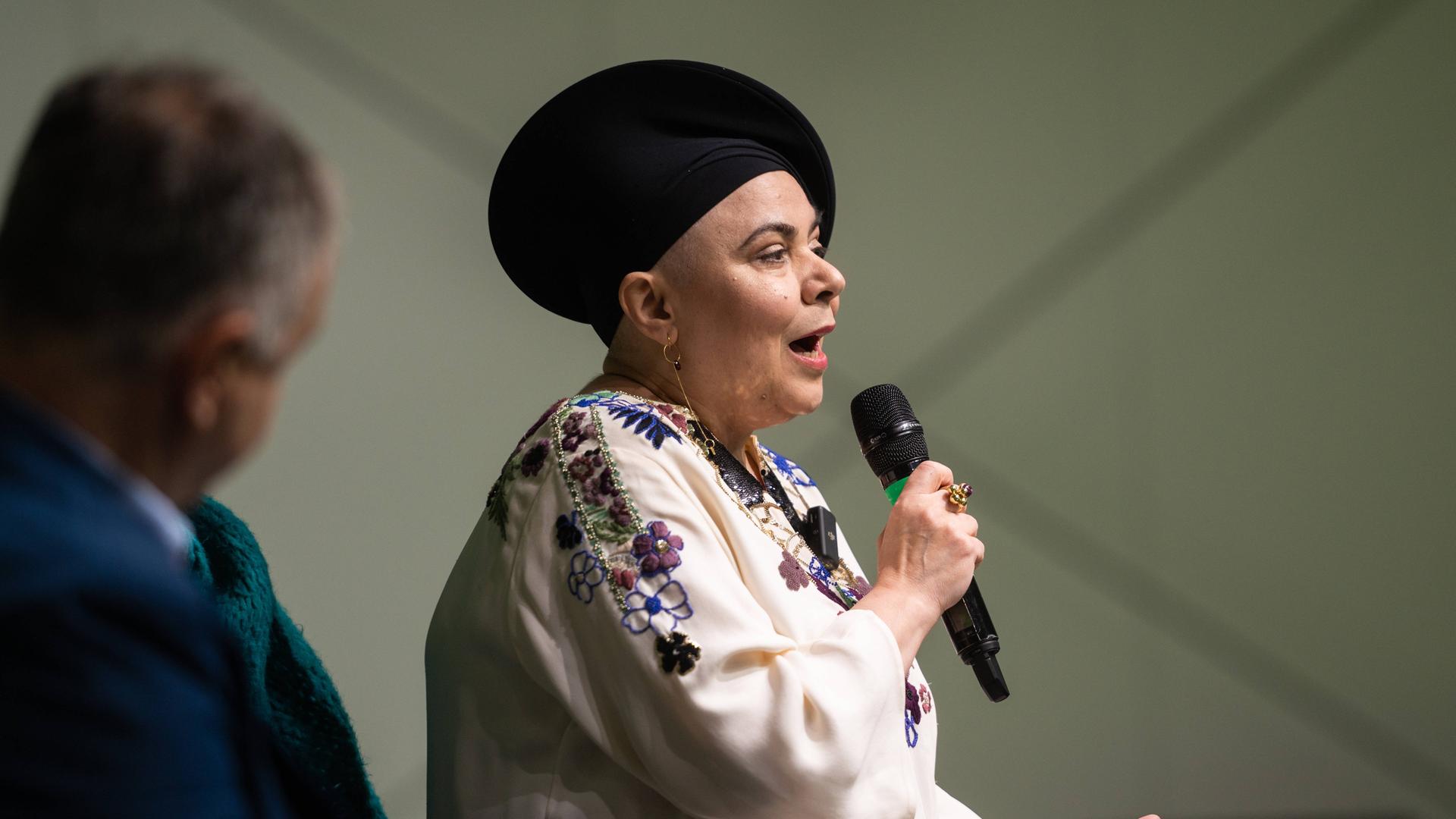 Die italienische Autorin Michela Murgia spricht in ein Mikro. Sie trägt eine blumenbestickte Bluse und einen schwarzen Hut.