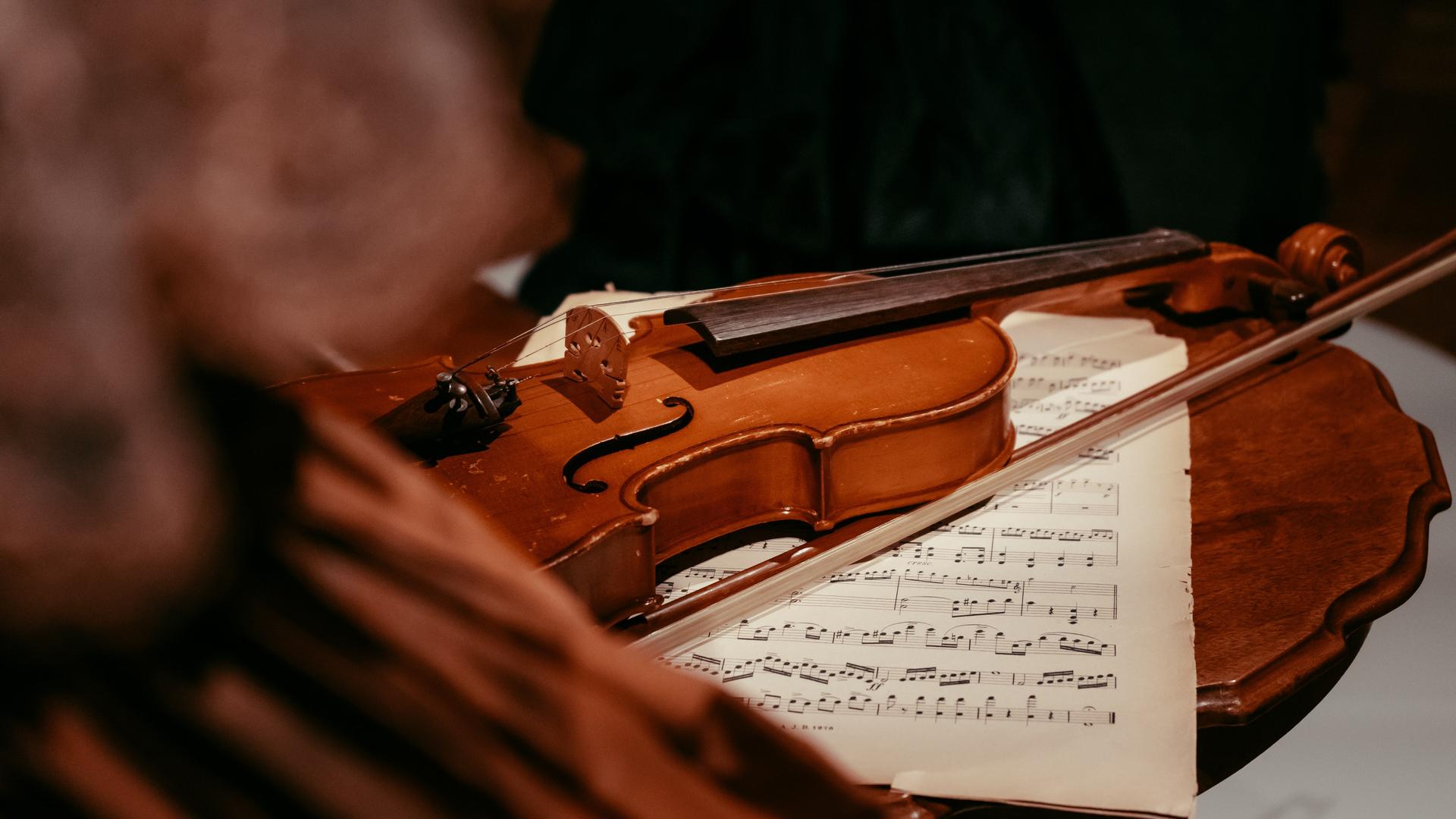Auf einem antiken Tisch liegen Notenblätter und eine Violine.