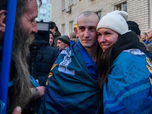 Ein Mann und eine Frau umarmen sich und blicken in die Kamera im Rahmen eines Gefangenenaustauschs zwischen Russland und Ukraine