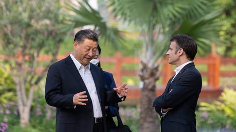 Chinas Präsident Xi und Frankreichs Präsident Macron reden in einem Garten miteinander, im Hintergrund sind Palmen zu sehen. Aufnahme vom 08.04.2023.