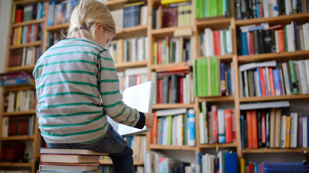 Ein Kind sitzt auf einem Buchstapel und liest ein Buch.