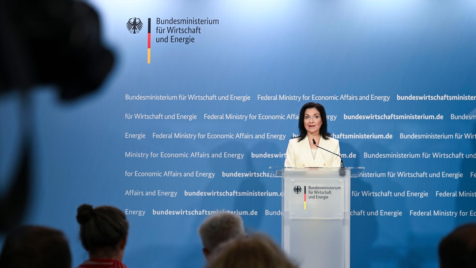 Reiche steht an einem Rednerpult uns sagt etwas. Hinter ihr eine blaue Wand mit auf dem Foto nicht lesbarer weißer Schrift. Reiche steht an einem Rednerpult uns sagt etwas. Hinter ihr eine blaue Wand mit auf dem Foto nicht lesbarer weißer Schrift.