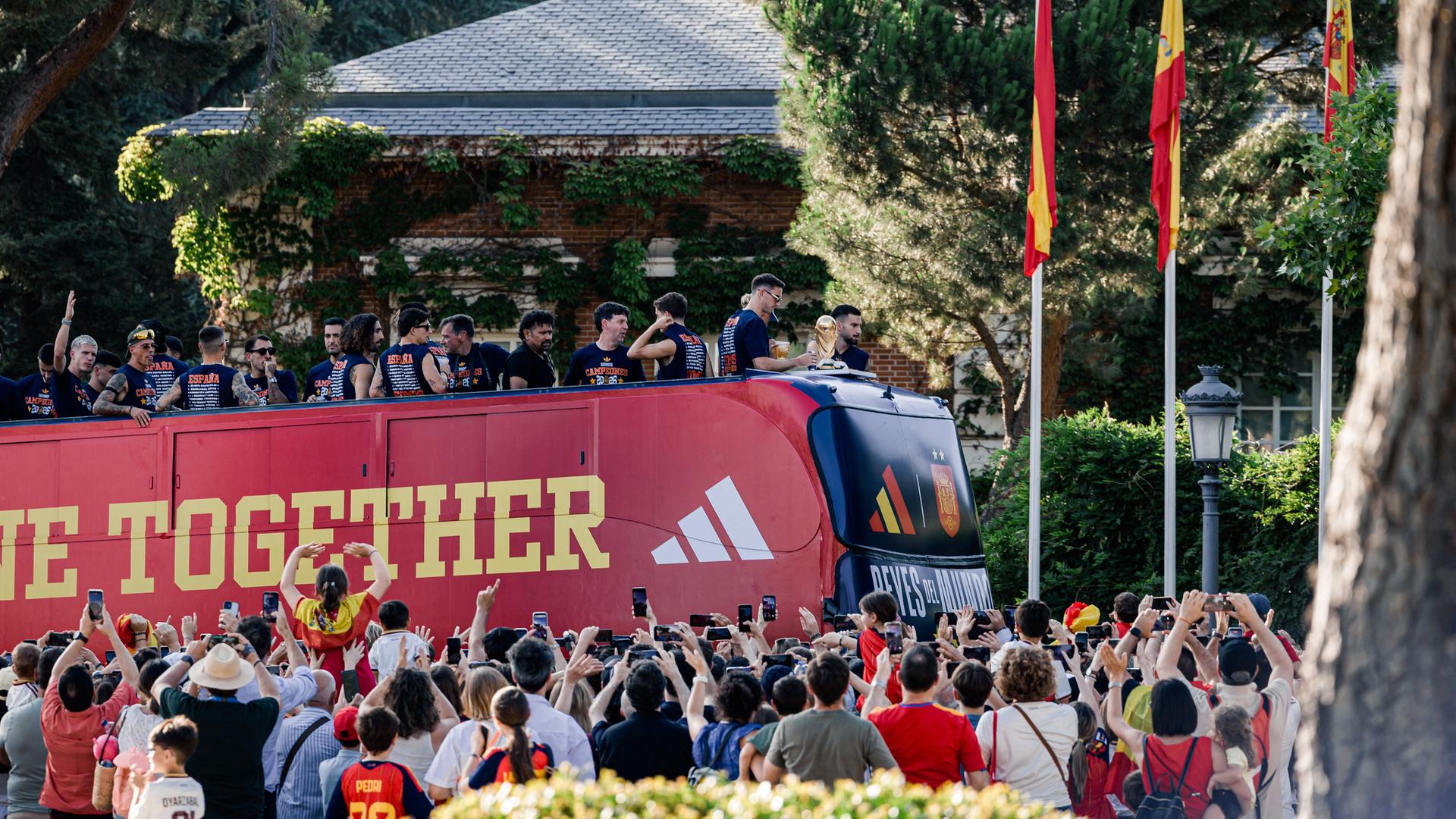 Die spanische Nationalmannschaft fährt mit einem offenen Bus durch Madrid. Fans stehen am Straßenrand, machen Fotos und jubeln.
Die spanische Nationalmannschaft fährt mit einem offenen Bus durch Madrid. Fans stehen am Straßenrand, machen Fotos und jubeln.